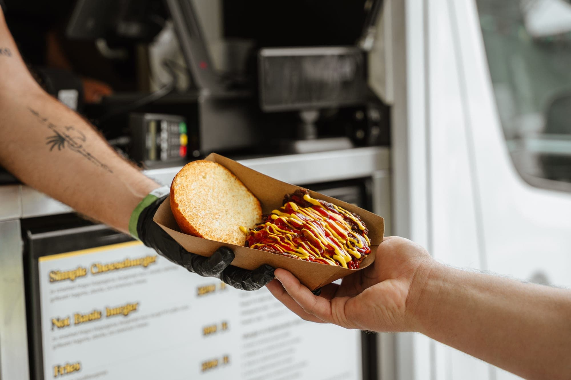 Átadás a food truck ablakánál: burger papírtálcán, a háttérben az árlap